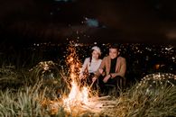 Smiling Asian couple basking near bonfire in evening