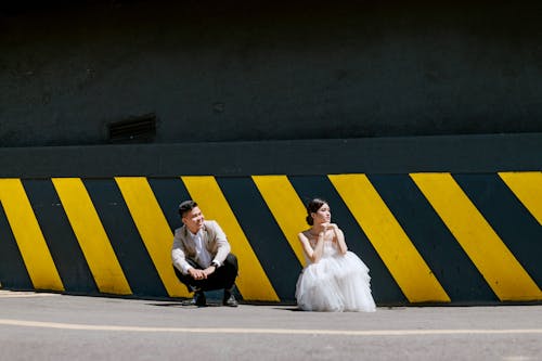 Stylish couple sitting on street near wall