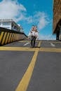 Cheerful young Asian man carrying woman in wedding dress on back on asphalt descent with yellow marking near modern building