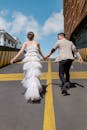 Cheerful couple in wedding clothes walking on asphalt road