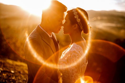 Side view of young ethnic couple in wedding clothes standing close in bright sunlight