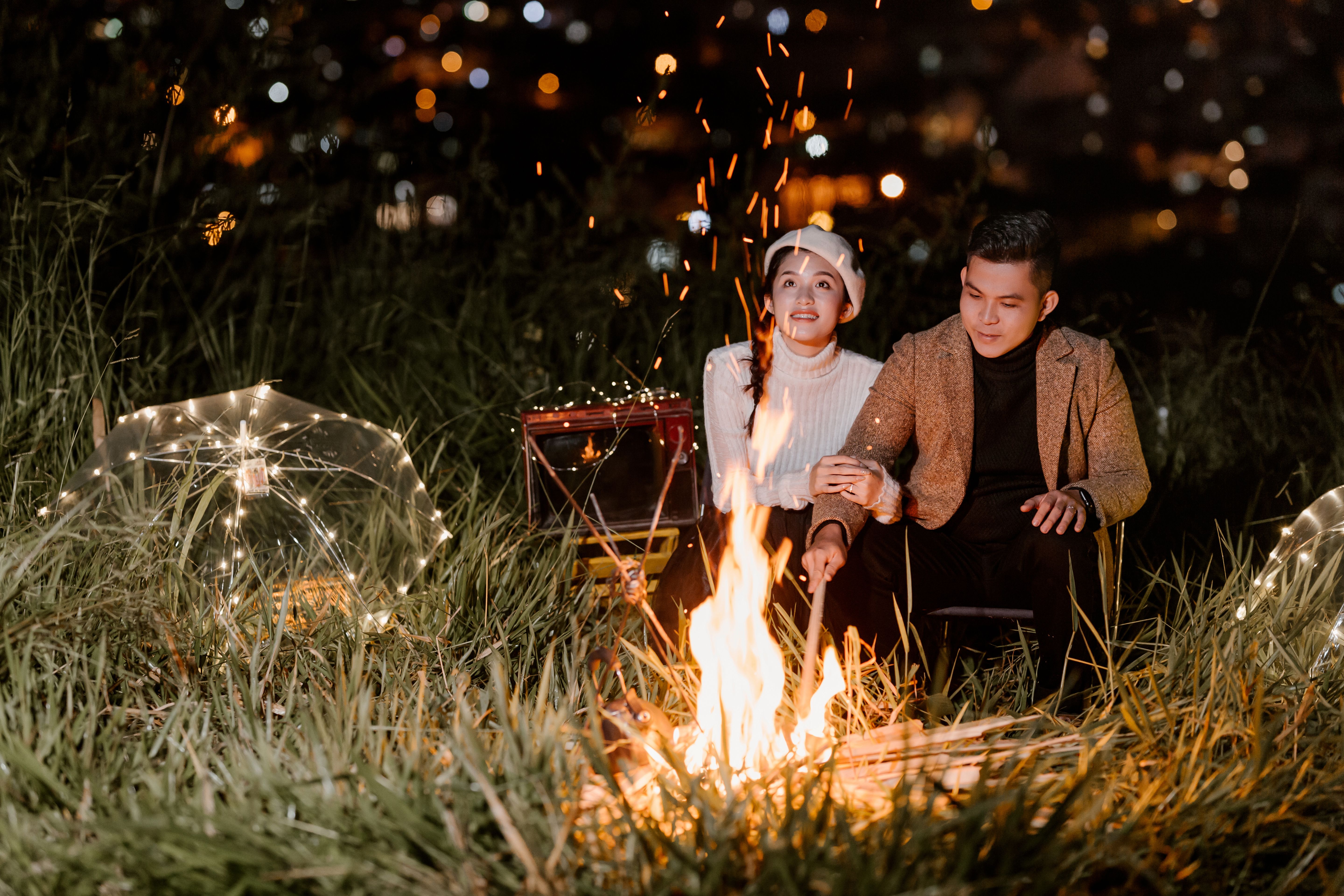 Ethnic couple sitting near burning fire in decorated field and looking at flame