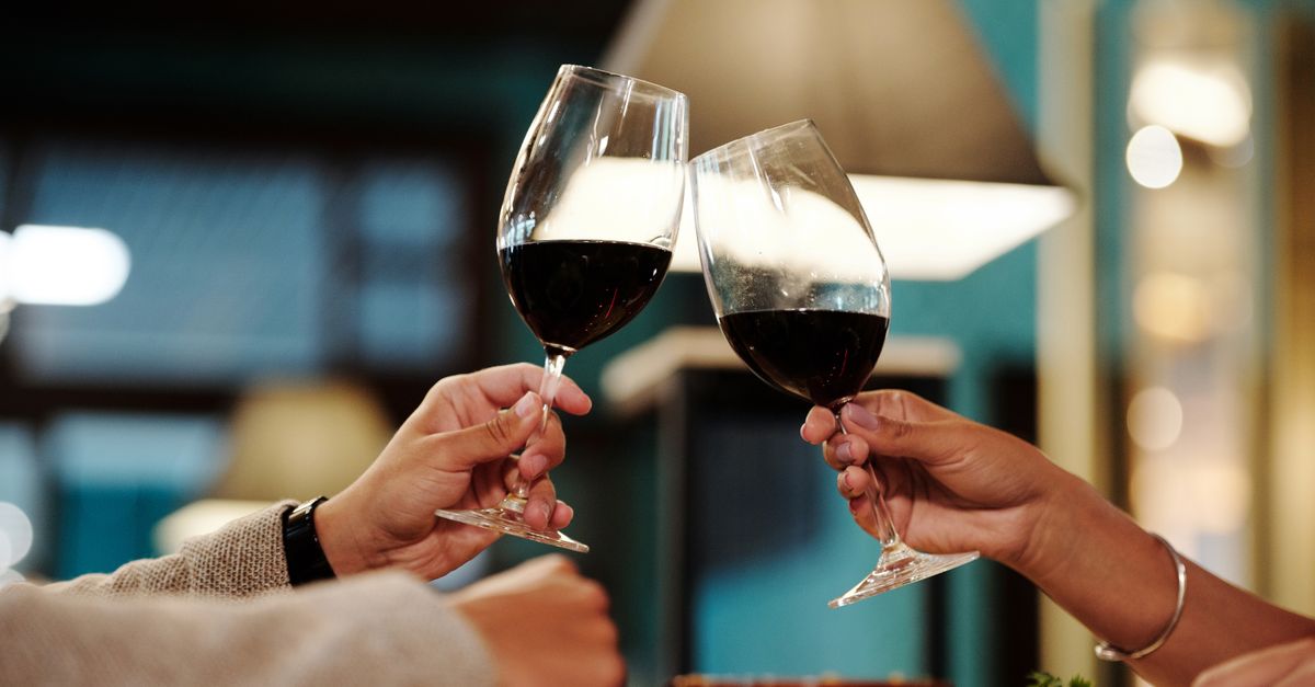 Two glasses of red wine raised at a dark restaurant table