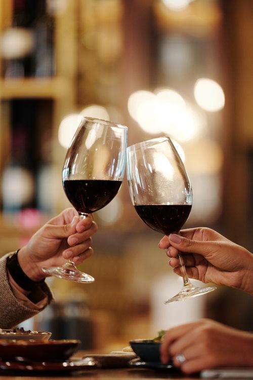 Free Close-up of two people toasting red wine glasses in a restaurant setting. Stock Photo
