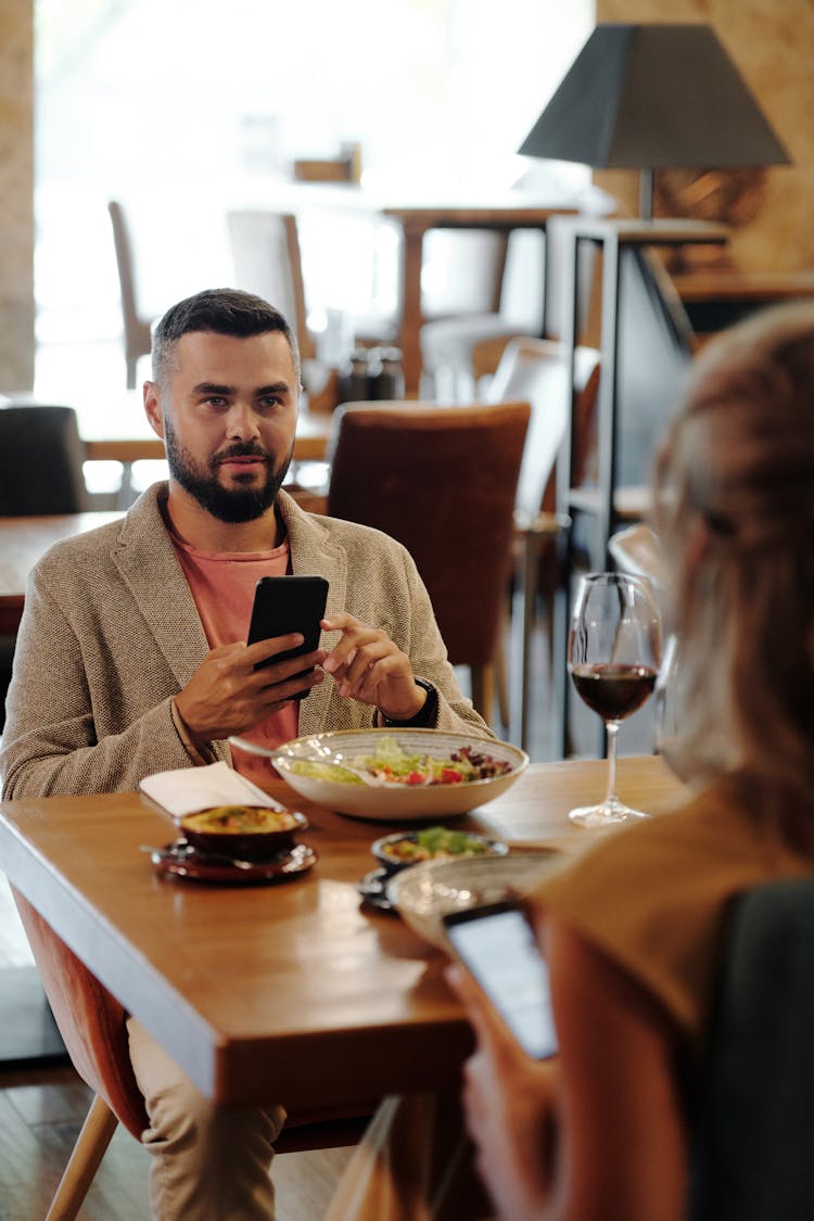 A Man And A Woman Having A Dinner While Busy Using Their Cellphones