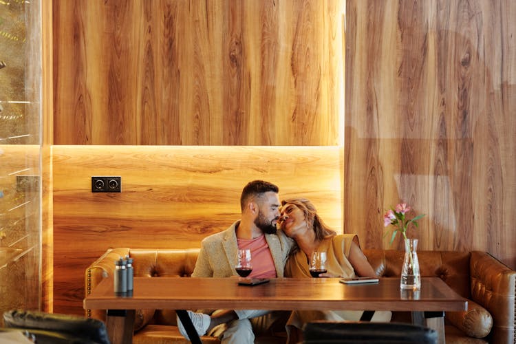 A Couple Sitting On A Couch Of A Restaurant While Looking At Each Other