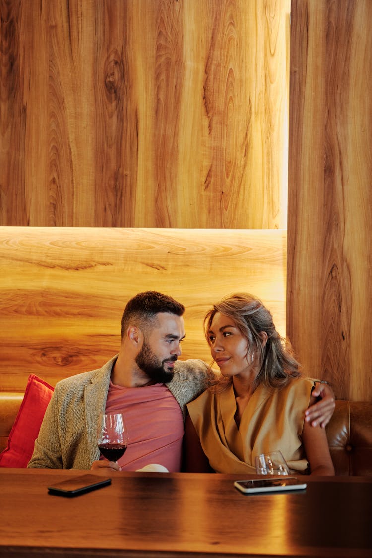 A Couple Holding Wine Glasses Sitting On A Couch While Looking At Each Other