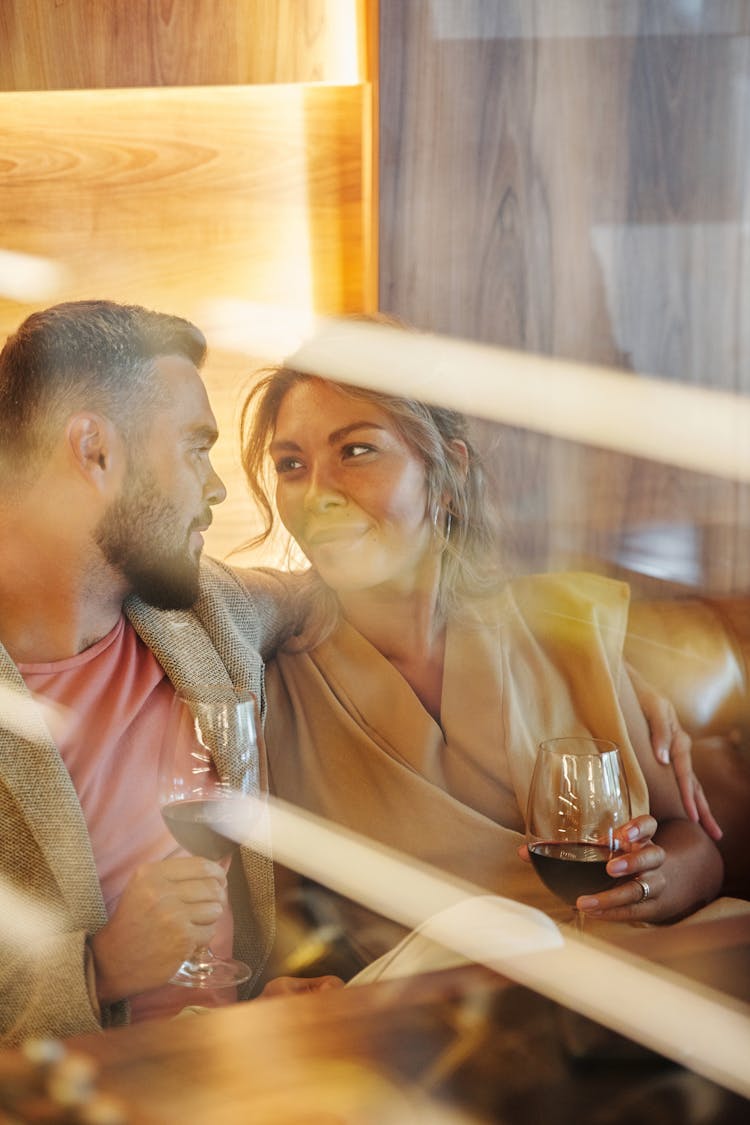 A Couple Holding Wine Glasses While Looking At Each Other