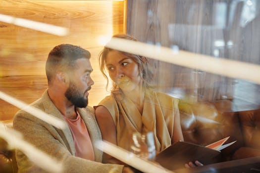 A couple enjoys a warm conversation in a cozy restaurant, viewed through a glass panel.