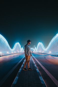 夜晚，一名男子站在一座现代化的灯光桥上，欣赏着城市的灯光