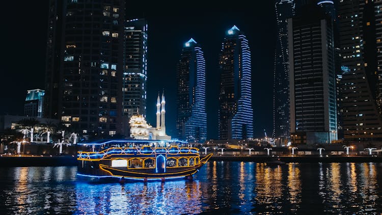 A Boat Sailing On River Near City Buildings During Night 