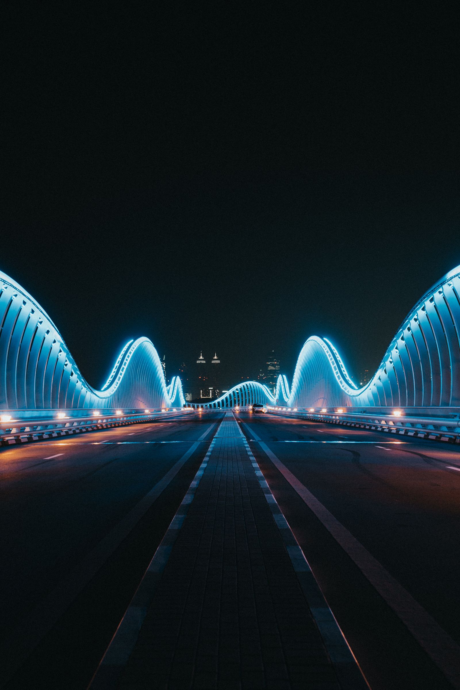 Night view along the Meydan Bridge, the blue-lit arches framing the road toward the distant Dubai towers.