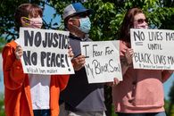 Multiethnic rebels in casual wear and medical masks standing with banners in city park while attending antiracist meeting