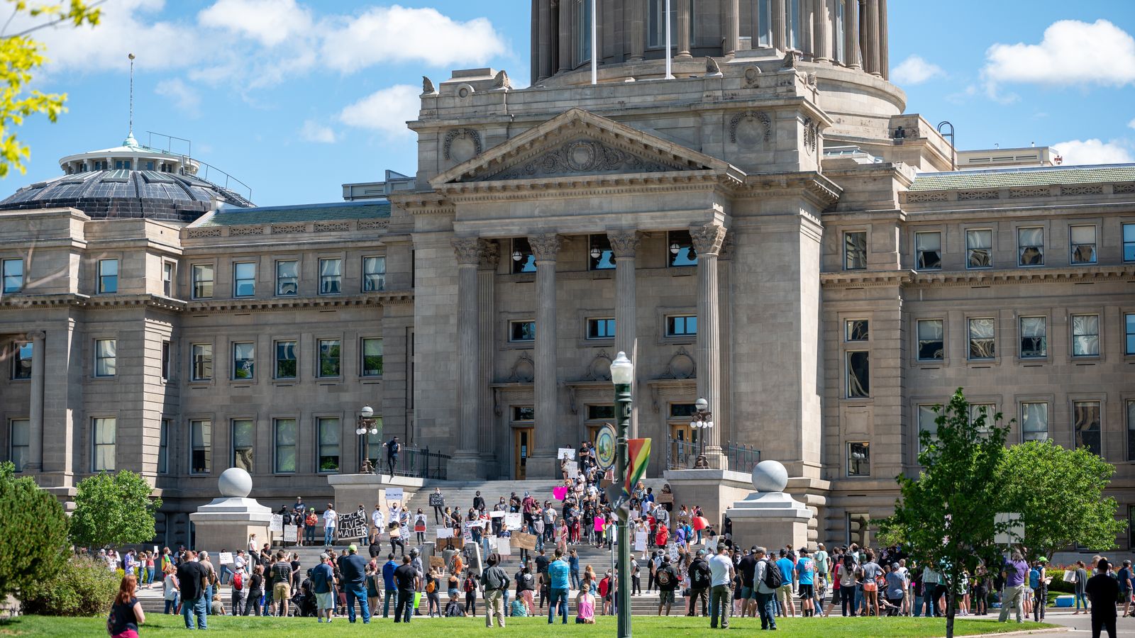 People gathering outside majestic Idaho State Capitol building for meeting on sunny day in Boise City