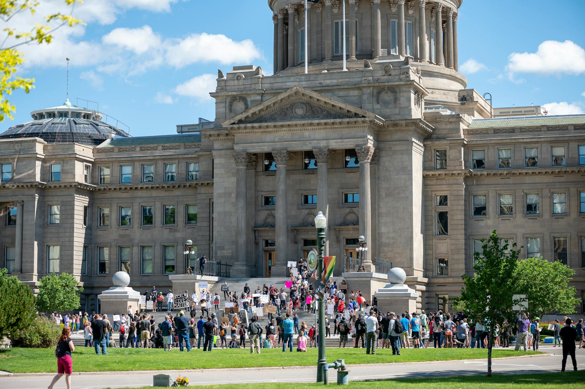 People gathering outside majestic Idaho State Capitol building for meeting on sunny day in Boise City