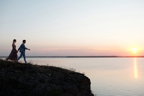 A Couple Holding Hands while Walking Near a Cliff