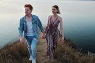 一对年轻夫妇手拉手，走在海边风景优美的悬崖小路上