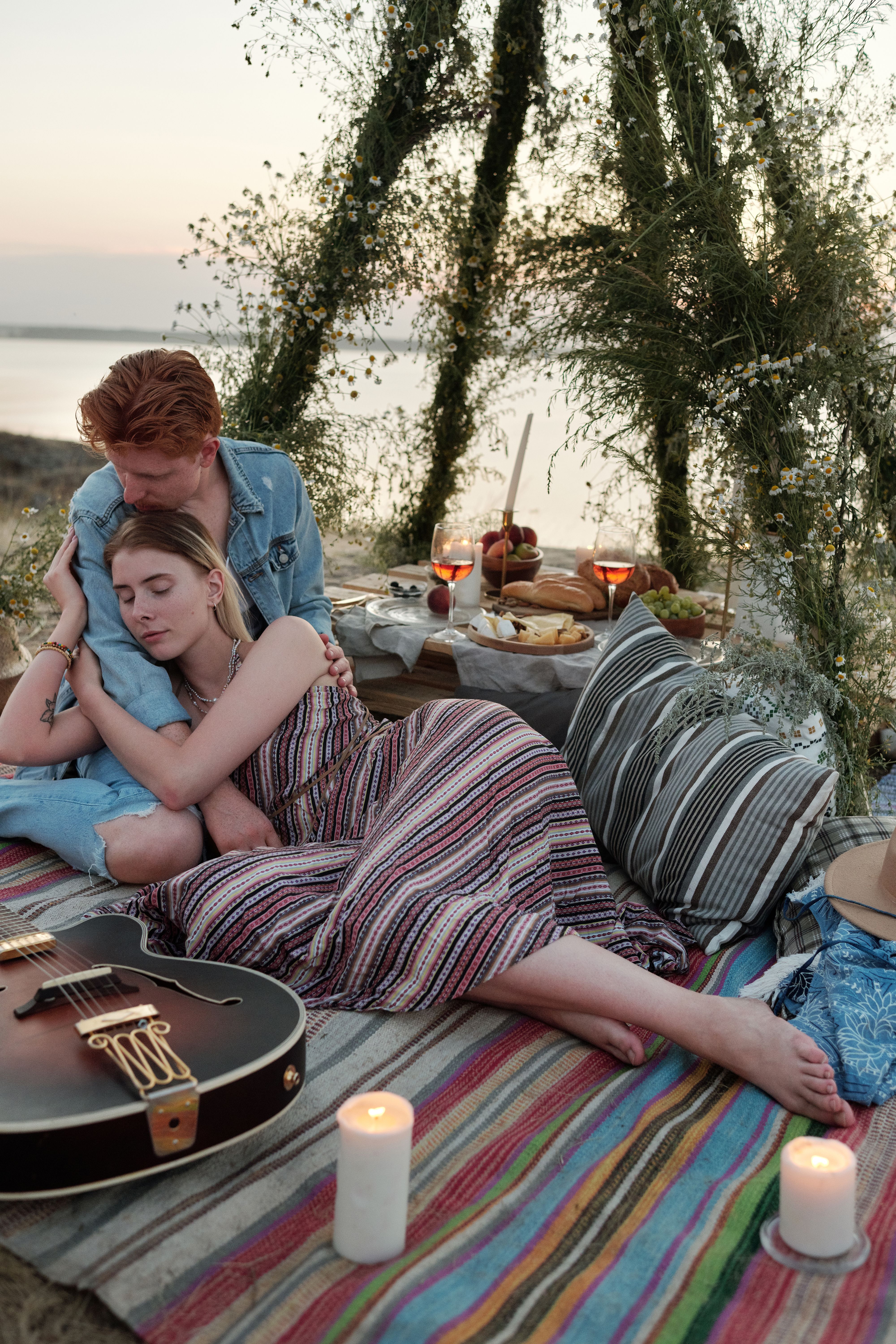 Couple enjoying a romantic sunset picnic on the beach with music and cozy decor.
