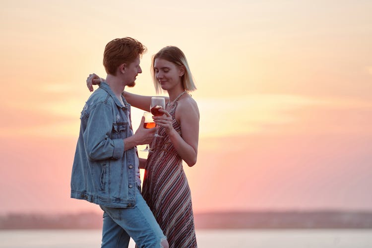 A Romantic Couple Holding Wine Glasses During Sunset