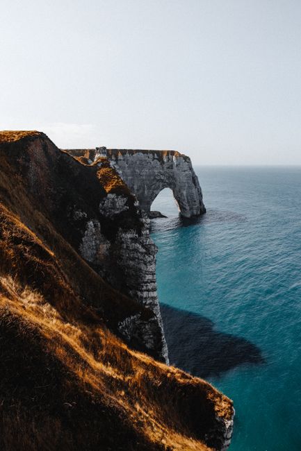 Stunning view of coastal cliffs and arch formation against a serene blue ocean, showcasing natural beauty.