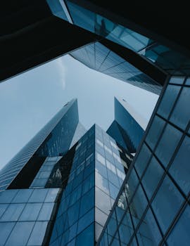 Low angle view of futuristic skyscrapers with glass facades against a clear blue sky.