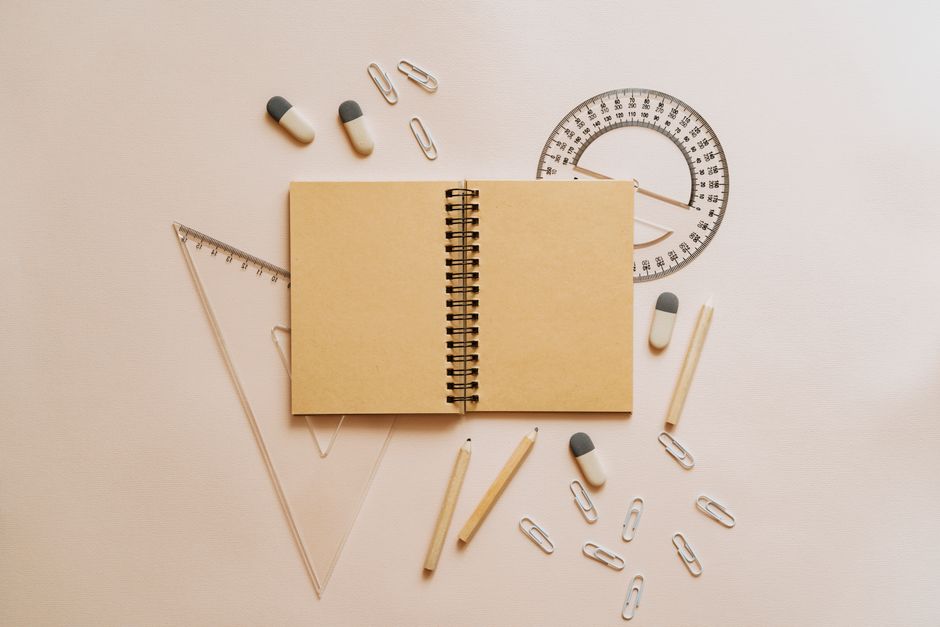 Flat lay of school stationery including a notebook, pencils, and geometry tools on a beige background.