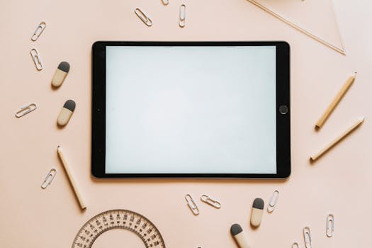 A tablet surrounded by stationery items like pencils, erasers, and paper clips in a flat lay setup.