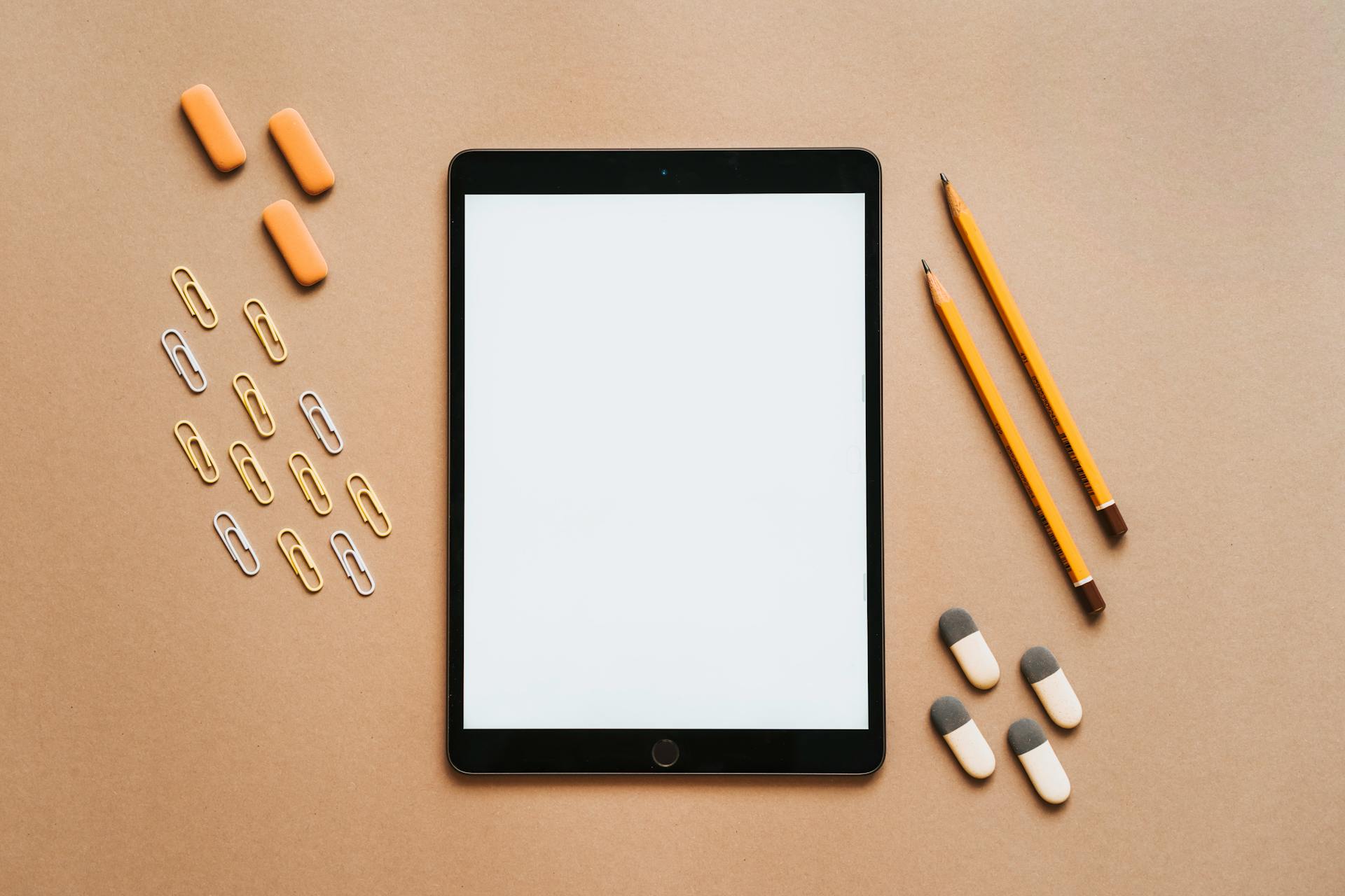 A minimalist flat lay of a tablet surrounded by school stationery on a beige background, perfect for educational themes.