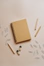 在米色的极简主义平面背景上，摆放着螺旋笔记本、铅笔、橡皮擦和曲别针