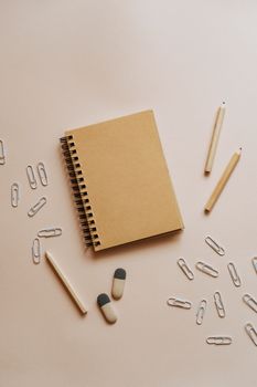 在米色的极简主义平面背景上，摆放着螺旋笔记本、铅笔、橡皮擦和曲别针