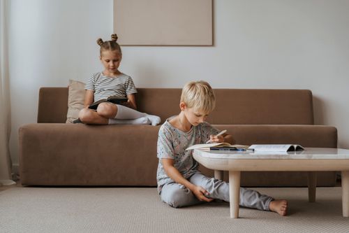 Free A boy studies while a girl relaxes on the sofa, both in a comfortable indoor room setting. Stock Photo
