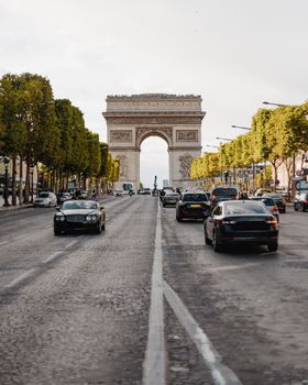 Iconic Arc de Triomphe with bustling traffic and trees lining the Champs-Élysées in Paris.