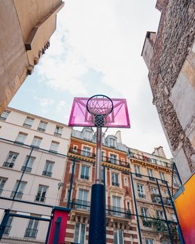 Low-angle shot of a pink basketball hoop amidst urban buildings, perfect for sports themes.