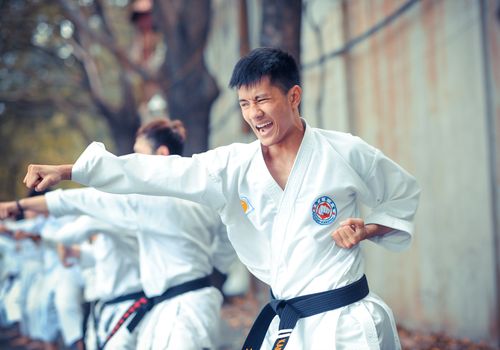 Asian man practices karate outdoors, showcasing skill and determination.