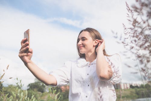 Close-Up Shot of a Pretty Woman in White Blouse Taking Selfie Using a Smartphone