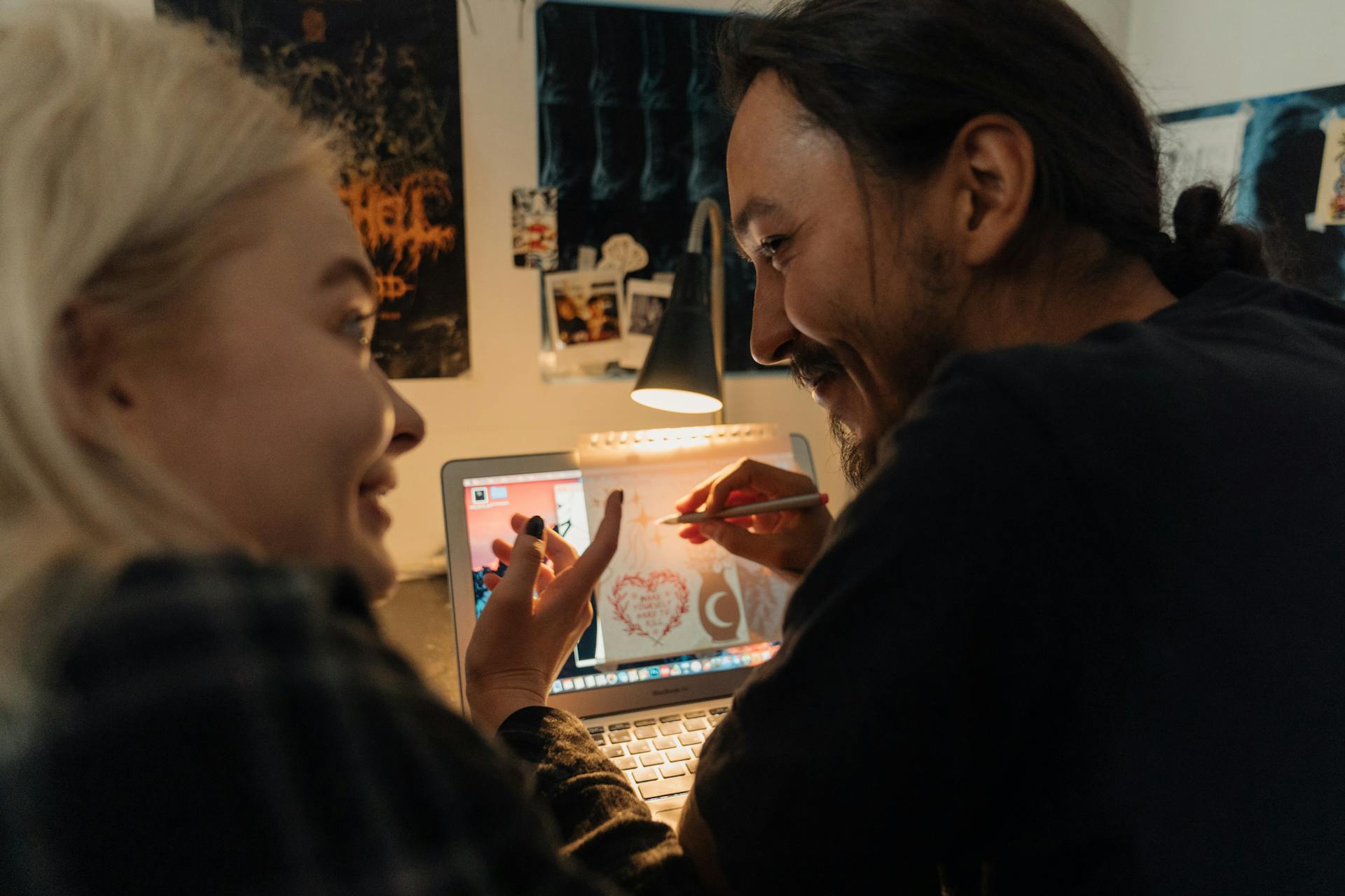 A couple collaborates on a digital art project on a laptop in a cozy home studio setting.