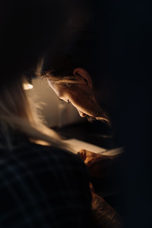 Free A man with long hair focuses on writing under warm dim light, giving a sense of creativity and concentration. Stock Photo