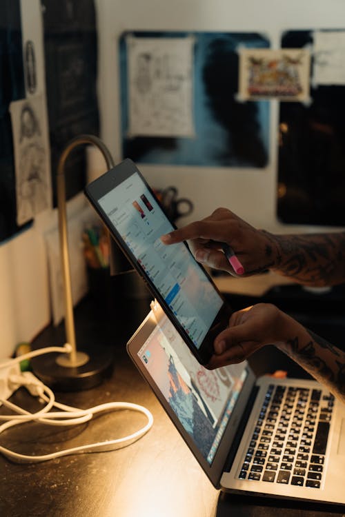 Person Holding Black Digital Tablet Near A Laptop