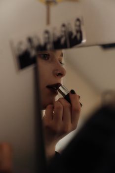 A woman applies lipstick while looking into a mirror, capturing elegance and style.