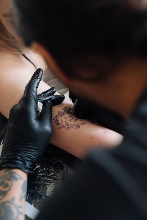 Free Close-up of a tattoo artist carefully inking a detailed design on a person's arm. Stock Photo