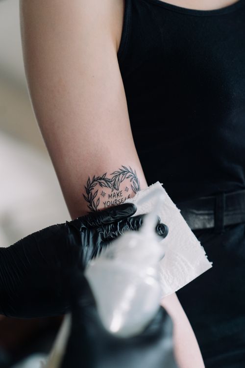 Free Detailed view of a tattoo artist applying a tattoo with black gloves, focusing on a text design. Stock Photo
