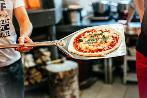 Person Holding Stainless Steel Spoon With Sliced Pizza