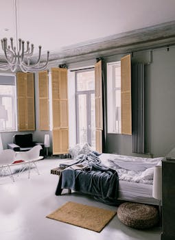 Sunlit minimalist bedroom featuring a chandelier, shutters, and elegant decor in Sankt-Peterburg.