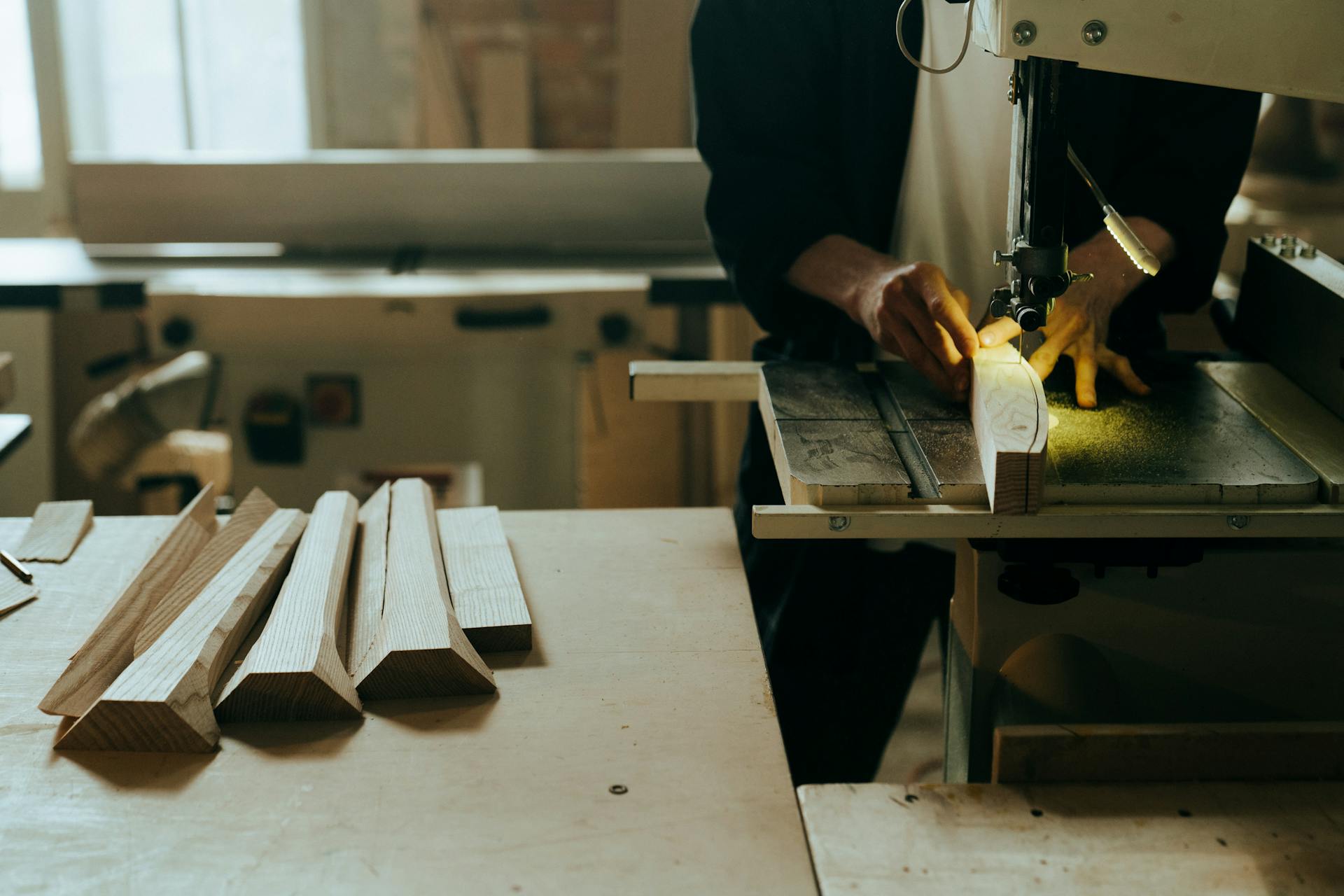 A craftsman operates a bandsaw, shaping wood in a well-equipped workshop.