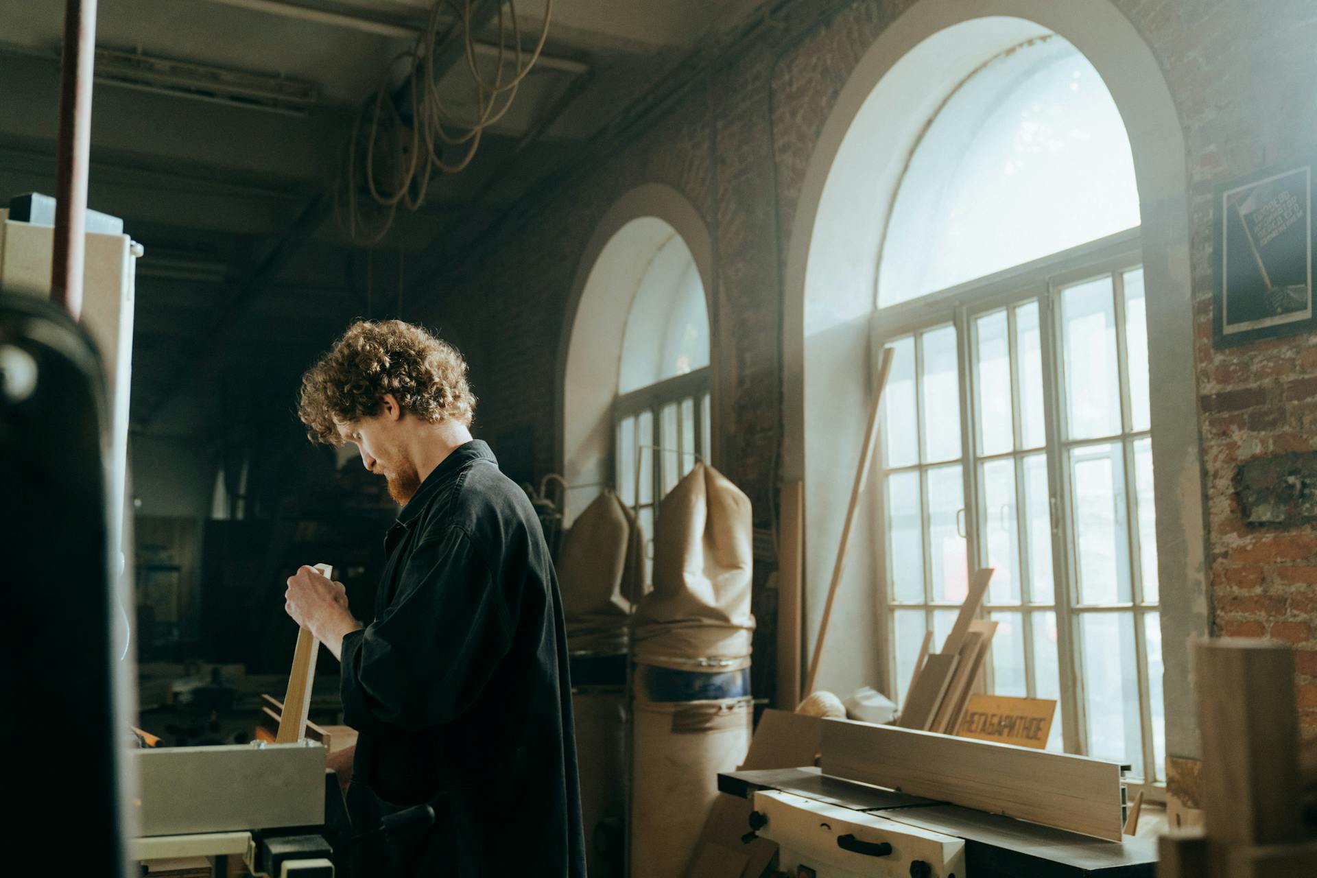 A focused craftsman works diligently in a sunlit, rustic workshop environment.