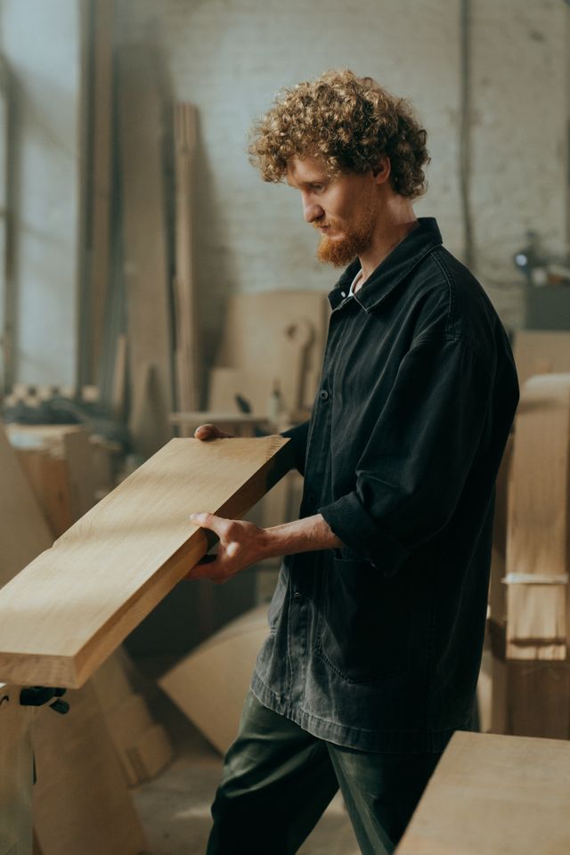 A furniture maker carrying a board across the workshop — photo by cottonbro studio on Pexels