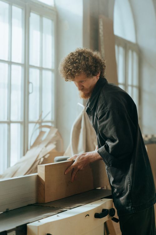 Free A curly-haired craftsman focusing on woodworking indoors in natural light. Stock Photo