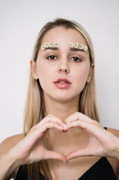 一位年轻女子神情安详，用手比出心形手势，眉间点缀着花朵