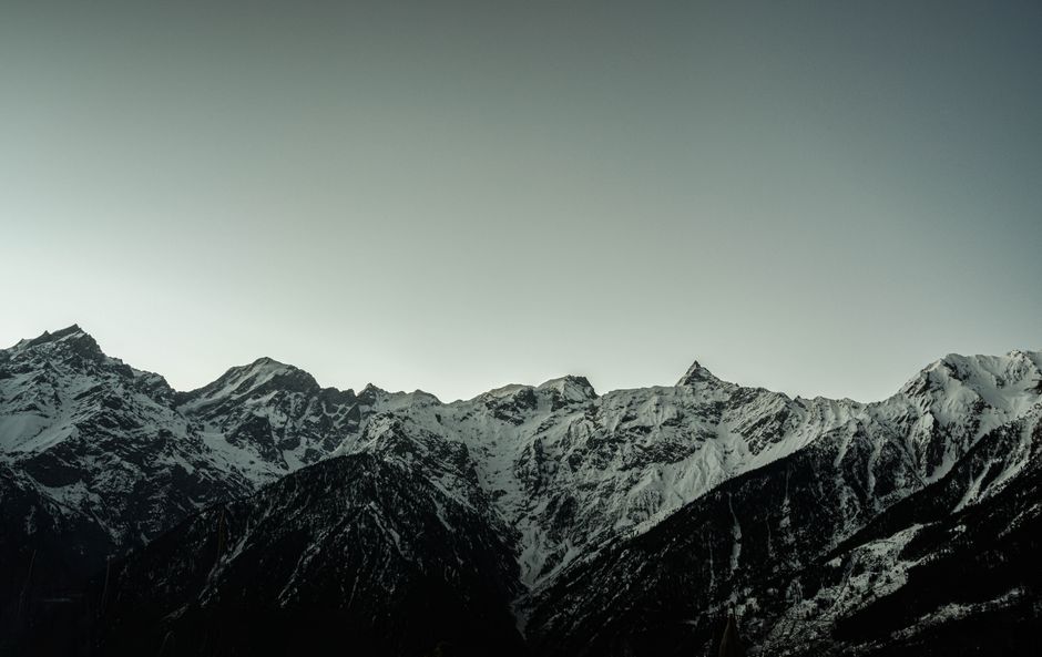 A stunning view of snow-covered mountain peaks against a gray sky, captured at dawn, showcasing nature's beauty.