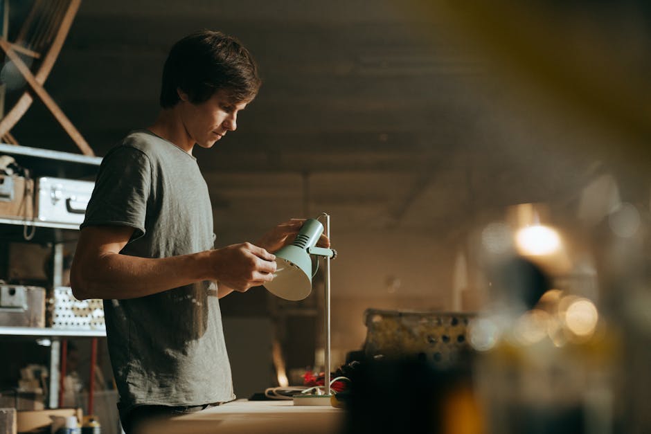 A young craftsman examines a lamp in his dimly lit workshop, focused and determined.